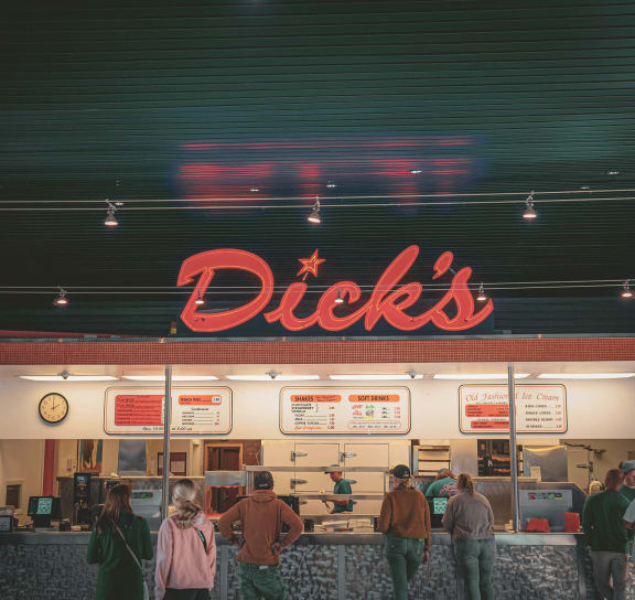 a group of people standing in front of a dicks fast food restaurant