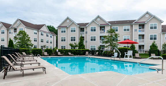A swimming pool surrounded by lounge chairs and umbrellas in front of apartment buildings.
