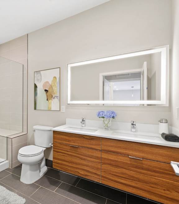 A modern bathroom with a glass shower stall, white toilet, and wooden vanity.