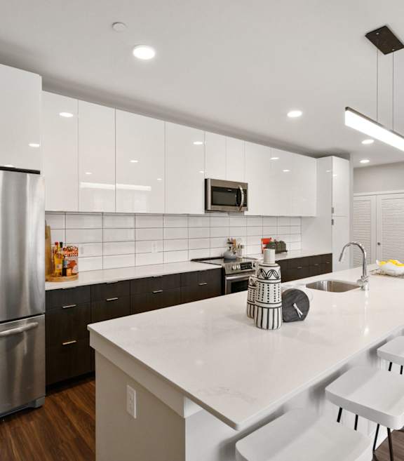 A modern kitchen with a long white counter and stainless steel appliances.