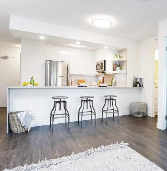 a kitchen with white cabinets and a bar with three stools