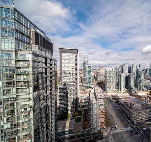 A cityscape with a mix of modern and older buildings, a construction site, and a partly cloudy sky.