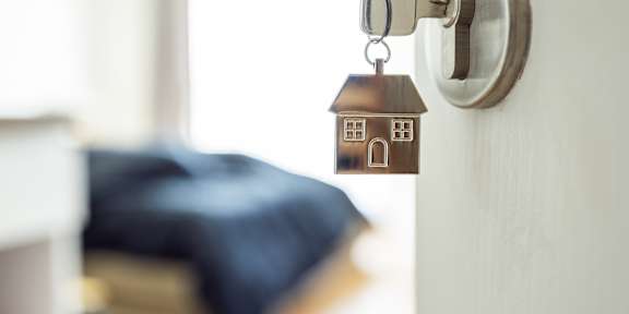 A key is inserted into a door lock with a keychain that has a house-shaped pendant.