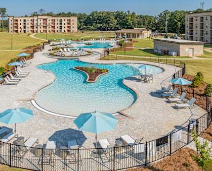 A large outdoor pool surrounded by a black fence and blue umbrellas.
