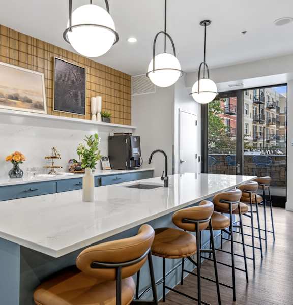 A kitchen with a long white island and brown bar stools.