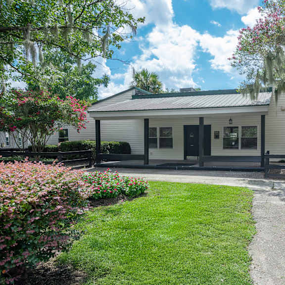 A white house with a green lawn and pink flowers in front. at Brackenbrook Apartments, North Charleston, SC