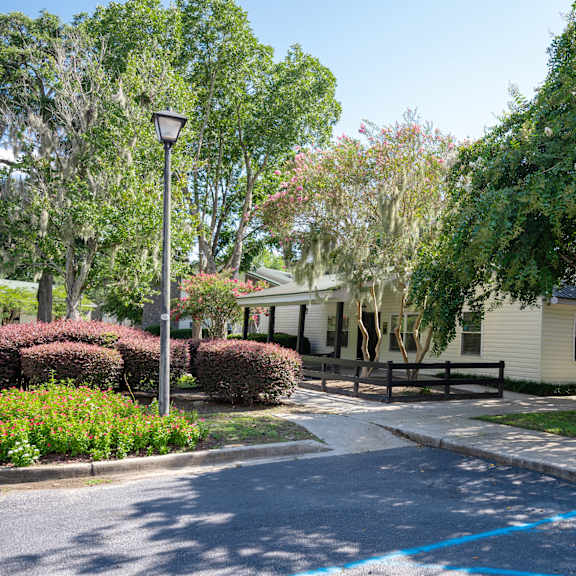 A white house is surrounded by green trees and bushes. at Brackenbrook Apartments, North Charleston 29418