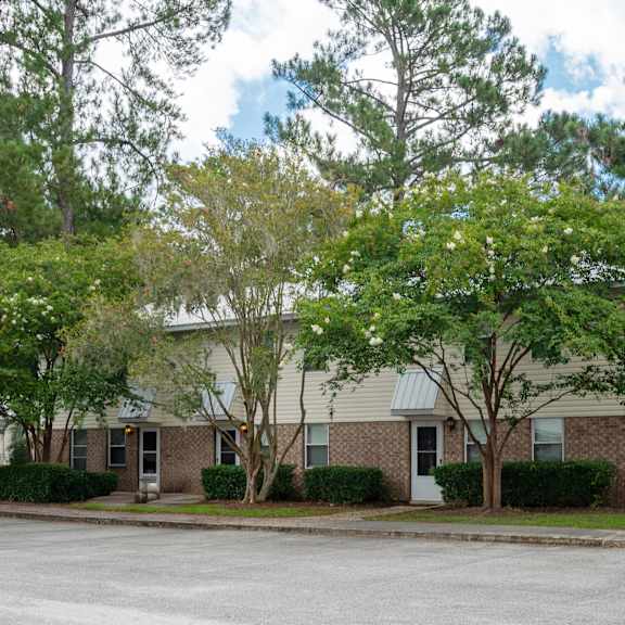 A building with a grey roof and a white door is surrounded by trees. at The Landing Townhomes Apartments, Hanahan, SC