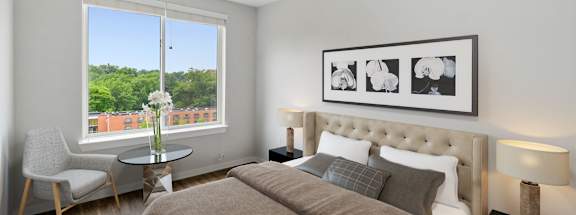 A bedroom with a large bed, a chair, a table, and a framed picture on the wall.