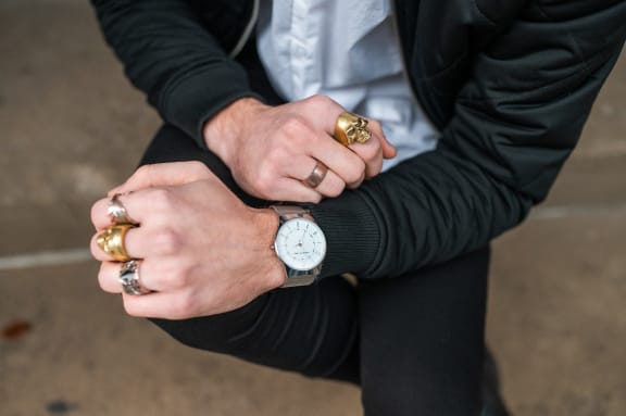 a man sitting with his hands crossed and wearing rings and a watch