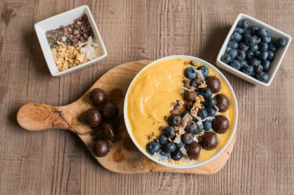 a bowl of mango smoothie with blueberries and nuts on a wooden cutting board
