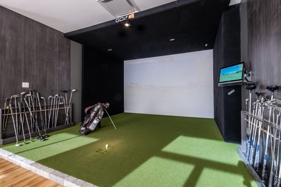 a golf simulator on a green carpet in a room with black walls and a television