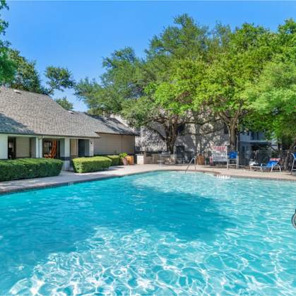 A swimming pool in front of a house with trees in the background.