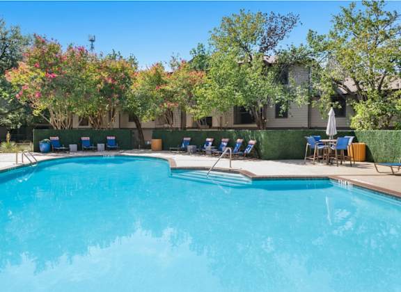 A swimming pool surrounded by trees and chairs.