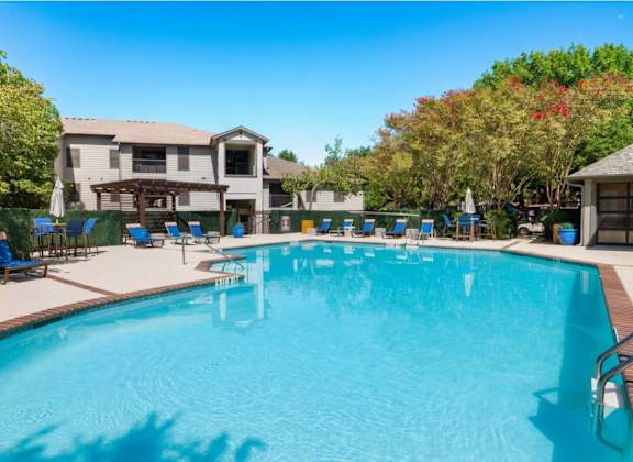 A large swimming pool in front of a house with a deck and lounge chairs.