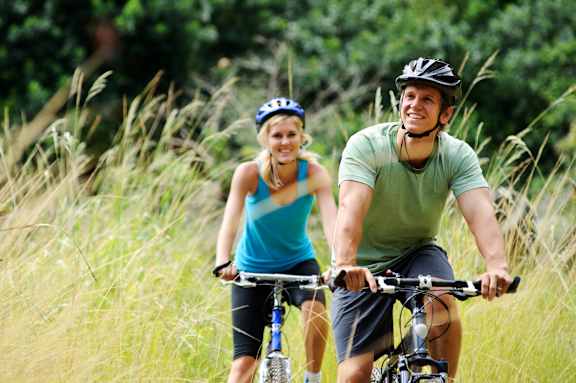 A man and a woman are riding bicycles in a field.