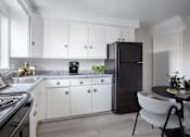 Thumbnail 3 of 3 - A black refrigerator stands in a kitchen with white cabinets and a marble countertop.