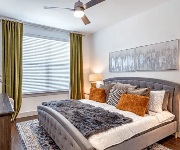 A bedroom with a bed, a ceiling fan, and a painting on the wall.