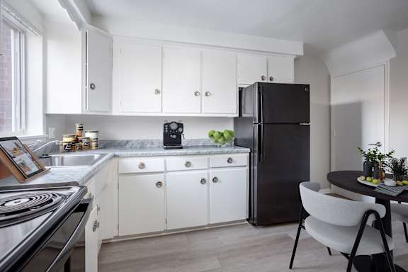 A black refrigerator stands in a kitchen with white cabinets and a marble countertop.