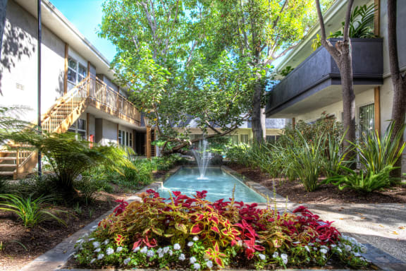 a courtyard with a fountain and a building with trees and flowers at West Park Village, Los Angeles, California