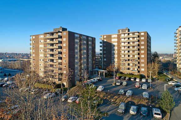 A parking lot with cars and three apartment buildings.