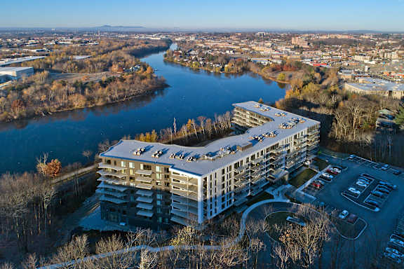 A large building with a flat roof is situated next to a river.