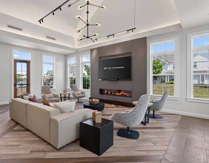 Clubhouse seating area with a sectional sofa, armchairs, fireplace, and tall windows.
