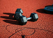 Thumbnail 1 of 4 - Two black dumbbells on a red rubber floor.
