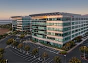 Thumbnail 4 of 12 - A modern building with a parking lot in front of it.