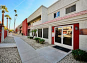 Thumbnail 2 of 8 - A building with a red door and windows is surrounded by palm trees.
