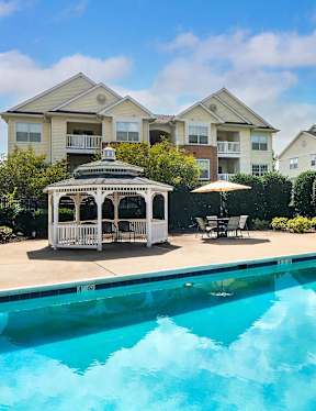 A swimming pool in front of a house with a gazebo.