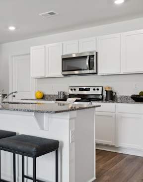 a kitchen with white cabinets and a bar with three stools
