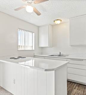 A white kitchen with a window and a ceiling fan. at Canyon Shadows Apartments, Riverside California