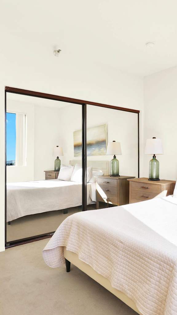 A bedroom with a large bed, a dresser, and a mirror. at Midvale Court Apartments Westwood, Los Angeles