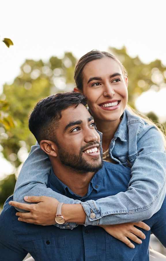 A man is giving a woman a piggyback ride in a park.