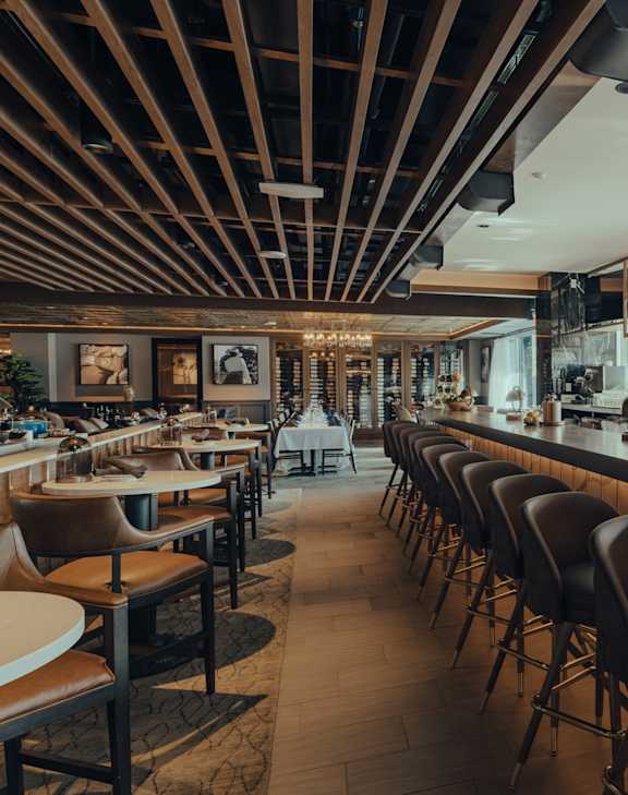 A bar with a long row of chairs and a shelf of bottles.
