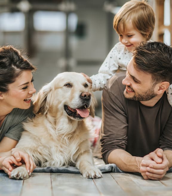A family of three is sitting on the floor with a dog.