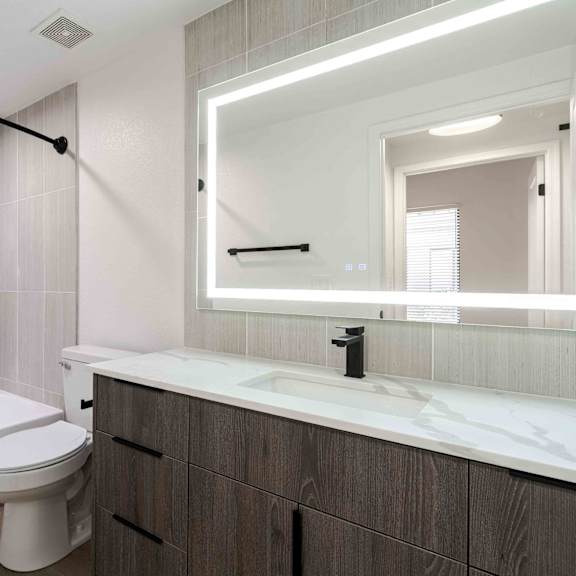 A white toilet sits in a bathroom with a white tub and a large mirror.