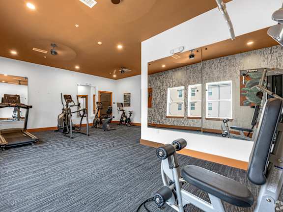 A gym with a variety of equipment including a treadmill, stationary bike, and weight bench.