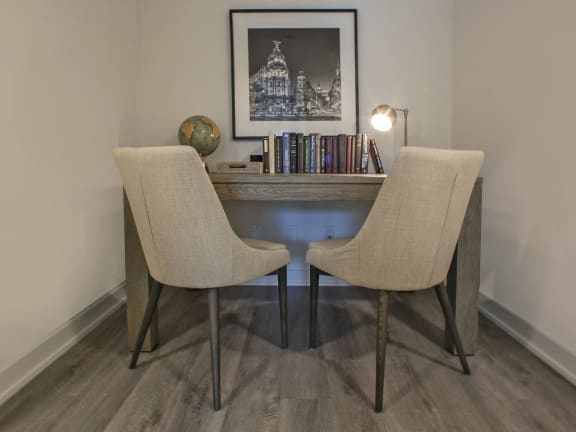 a desk with two chairs in a room with a bookshelf and a picture