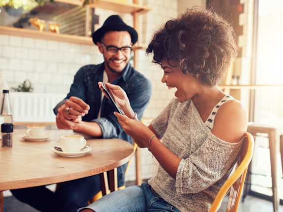 A man and a woman are sitting at a table in a cafe, with the woman looking at her phone.