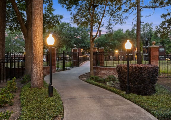a walkway through a park with lamps and a fence