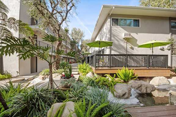 A patio with a table and chairs is surrounded by green plants.