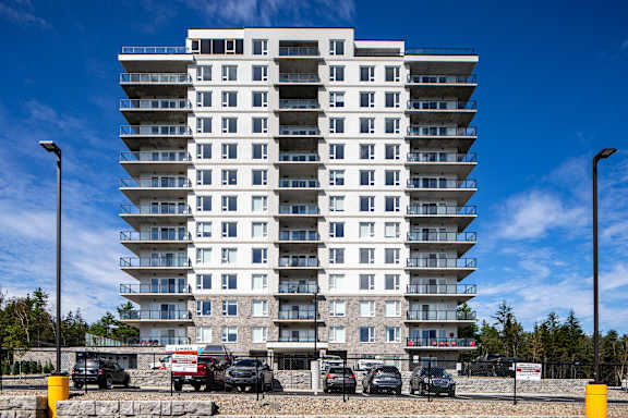A tall white residential building with cars parked in front.