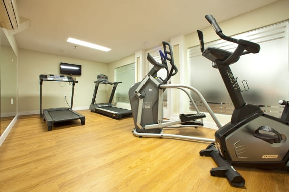 a gym with cardio equipment and a tv on the wall