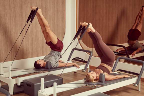 Two people doing pilates on reformers in a wooden room.
