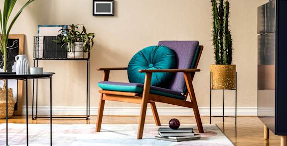 A chair with a teal cushion is in the center of a room with a table and a cactus.