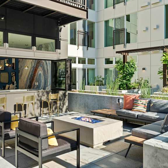 A patio with a table and chairs is surrounded by a concrete wall and a building.