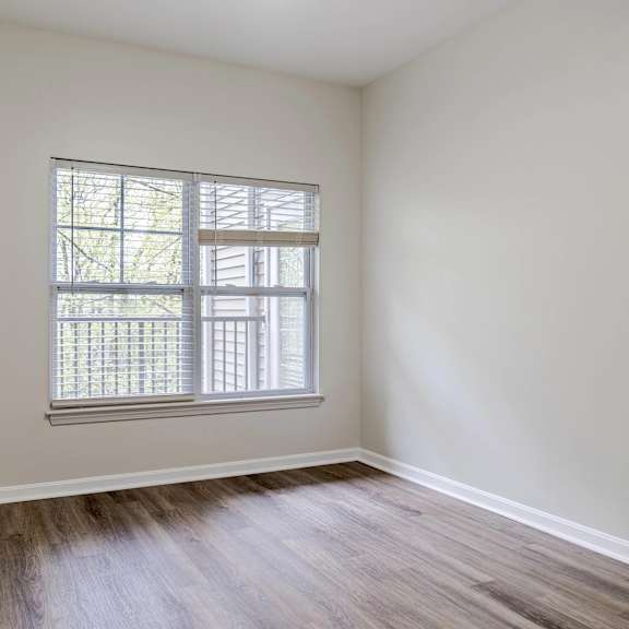 a bedroom with white walls and a window and wood floors