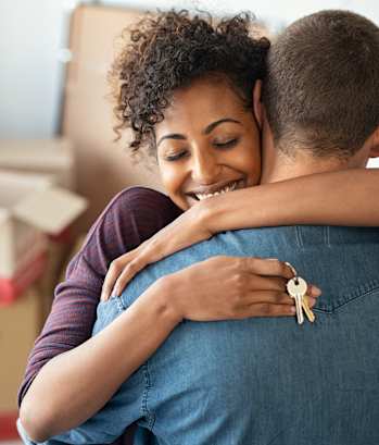 A couple hugging each other in a room with boxes in the background.